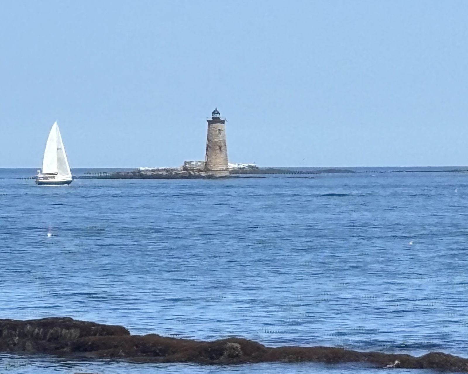 A lighthouse and a lone sailboat off Odiorne Point, New Hampshire.