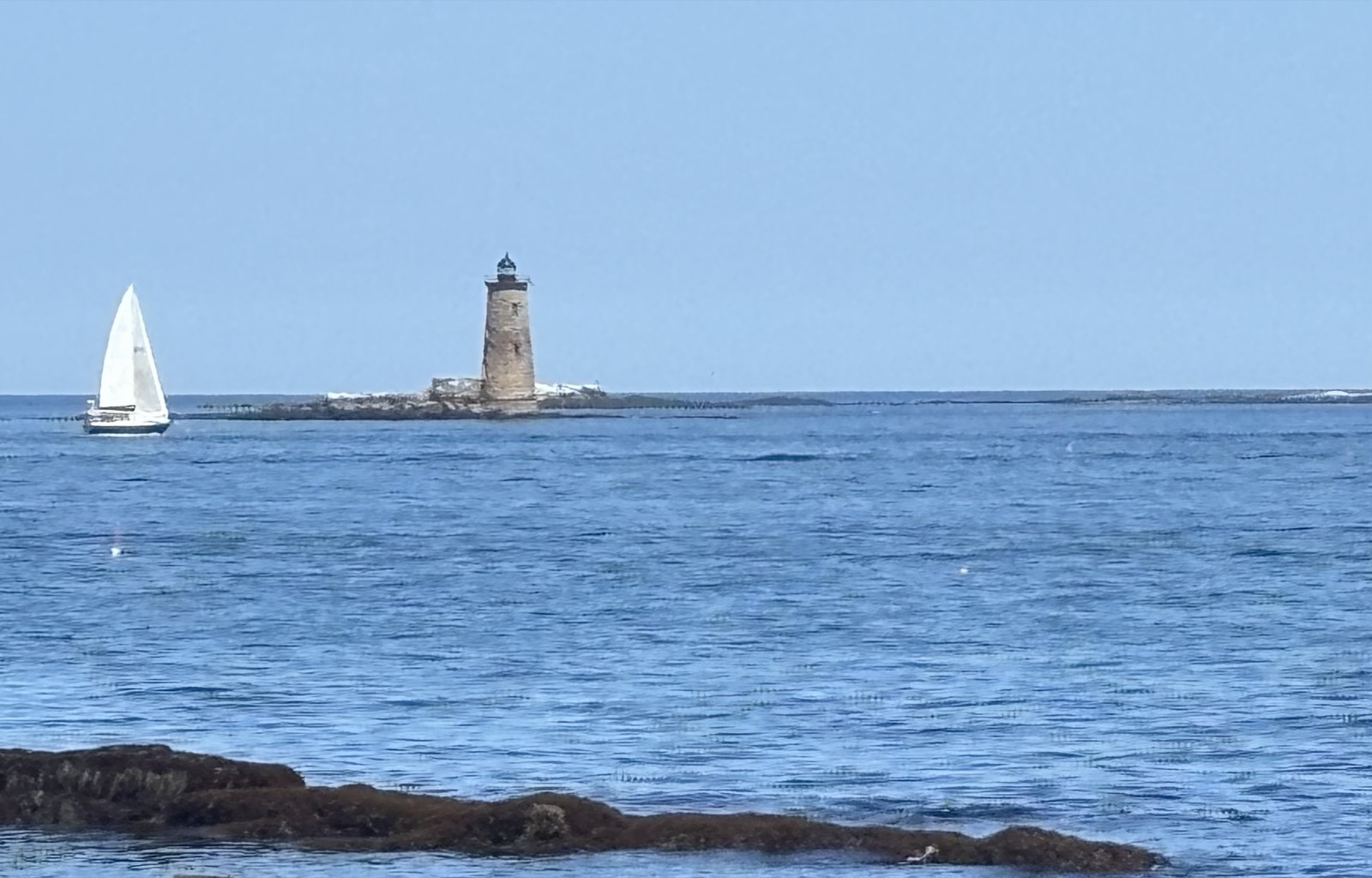 A lighthouse and a lone sailboat off Odiorne Point, New Hampshire.